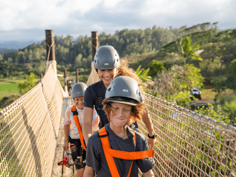 family of zipliners walks across a suspension bridge at CLIMB Works