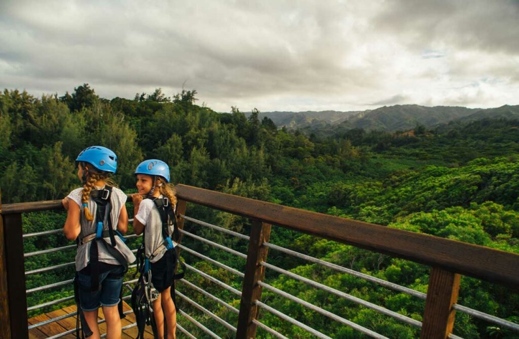 Two young girls watch others zipline on the North Shore waiting in excitement