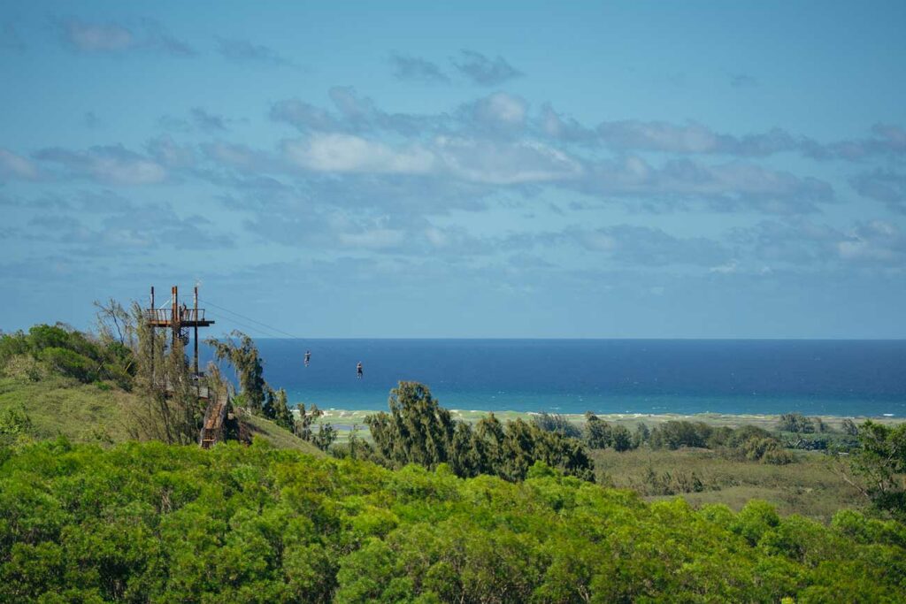 Zipliners zoom across a perfect day on the North Shore of Hawaii with green landscapes, blue skies and water