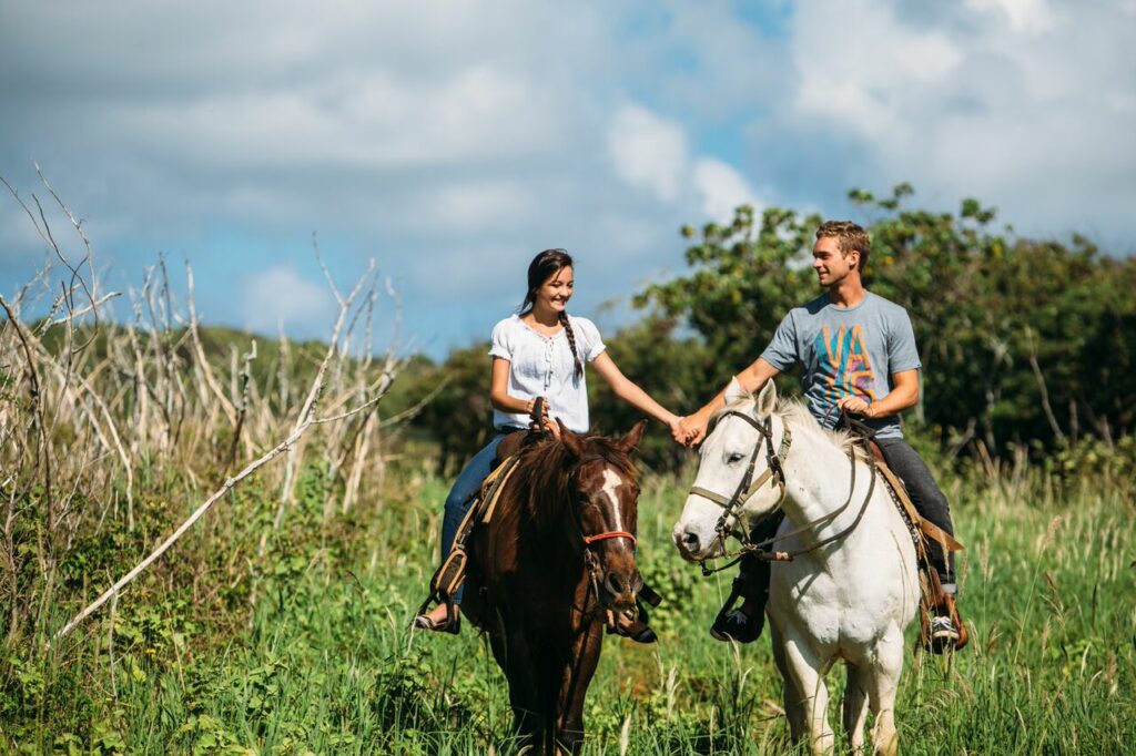 A couple holds hands on a scenic horse ride at Gunstock Ranch