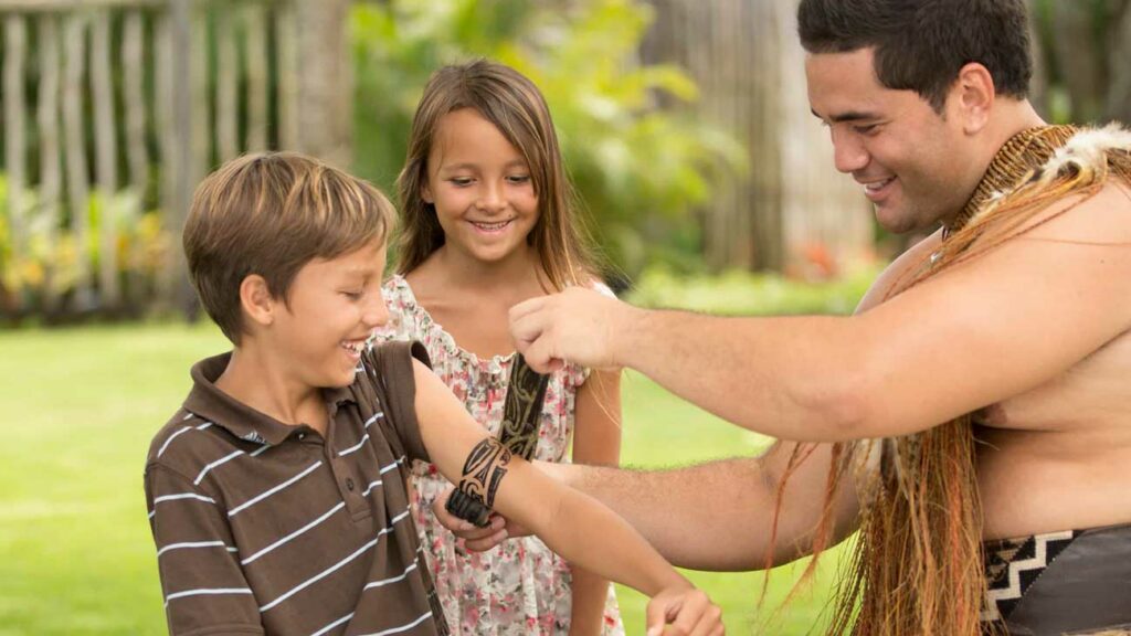 A staff member in the Aotearoa village at the PCC places a tattoo on children
