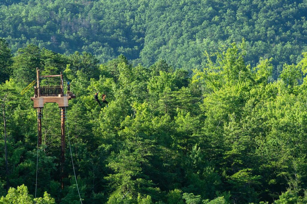 Visitors take off from a zipline platform on a dual zipline in the lush green landscape of the Smoky Mountains
