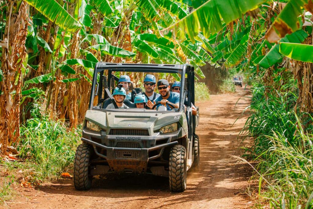 Guests smile as they take a UTV tour beneath the trees in Keana Farms