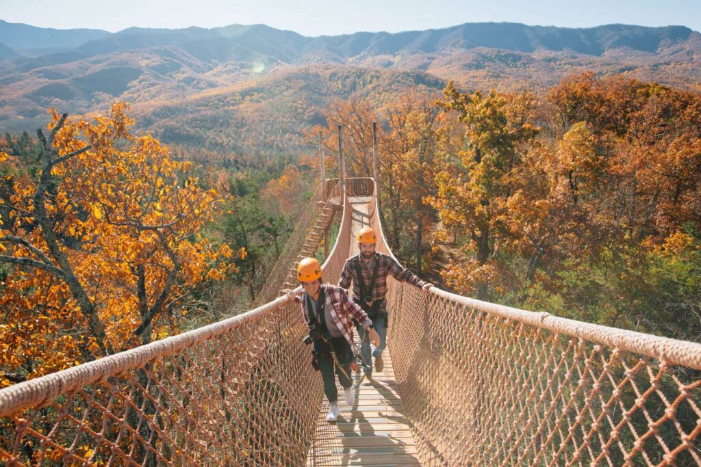 A couple in matching flannel cross a skybridge above the Smoky Mountains' fall colors