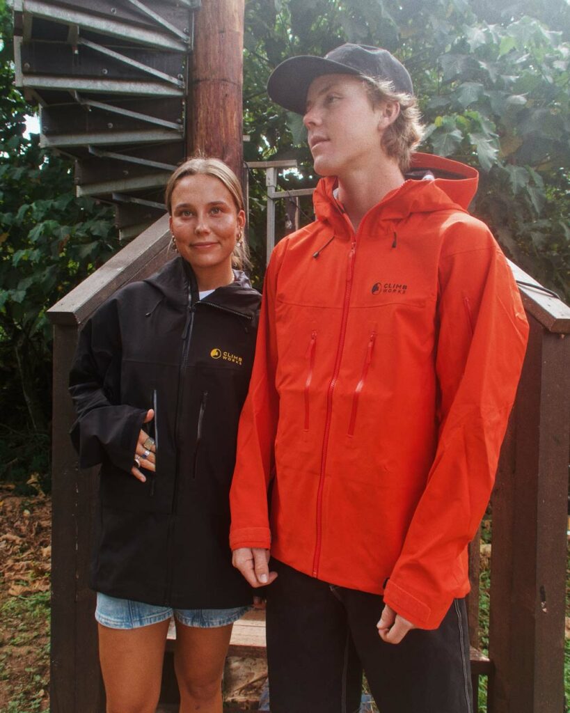 A man and a woman showcasing their CLIMB Works rain jackets at the bottom of a spiral staircase