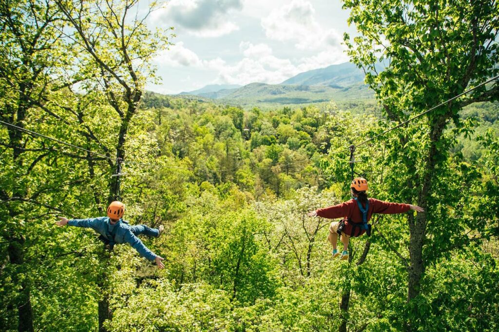 A man and woman zip line through lush green mountains in the Smokies